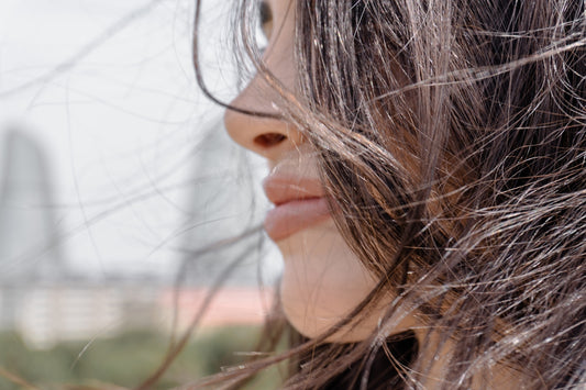 Woman's profile with wind-blown hair and blurred city background.