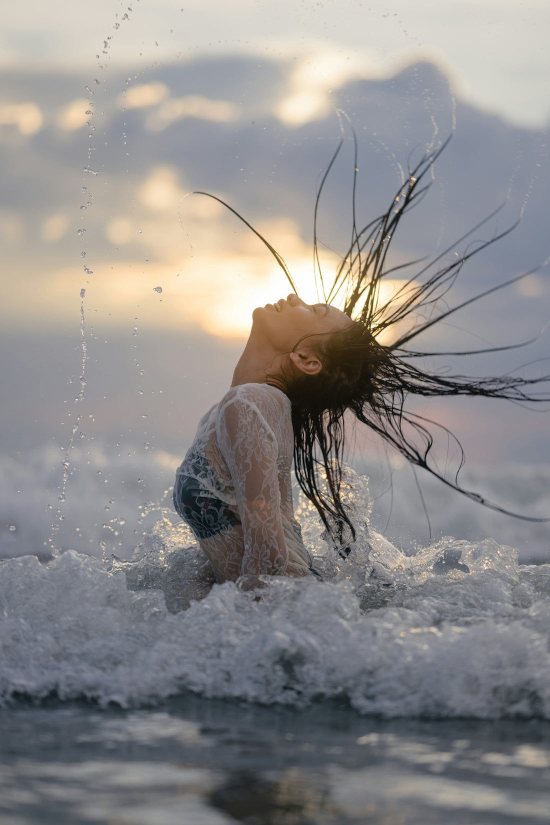 Young woman splashing water with hair at sunset.