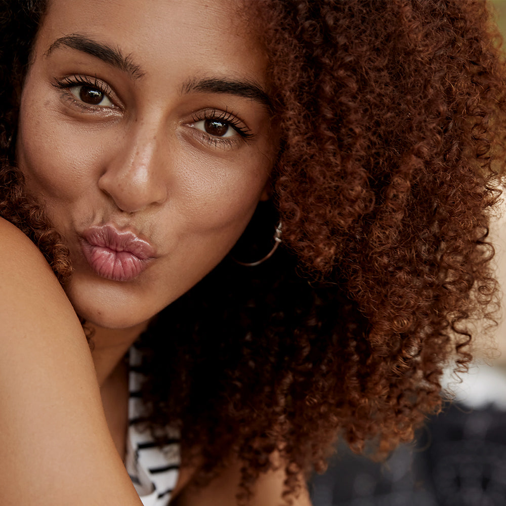 Close-up of a woman with curly hair blowing a kiss.